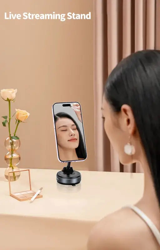 Woman using a live streaming stand with a phone on a table, with a vase of flowers and a candle in the background.